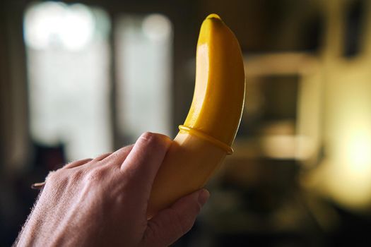 Yellow Condom and yellow banana holding a male hand indoors