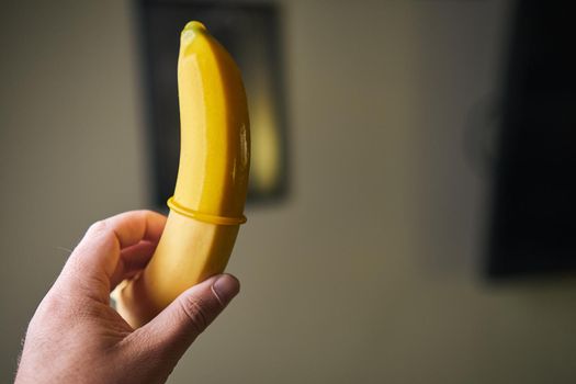 Yellow Condom and yellow banana holding a male hand indoors