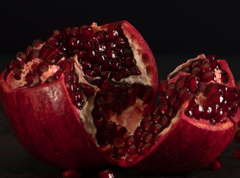 fresh open pomegranate with seeds on a black background. The red fruit is ready to eat. Peeled juicy fruit. High quality photo