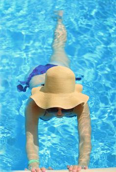 girl in a hat and sunglasses in the pool. Holds the side of the pool .