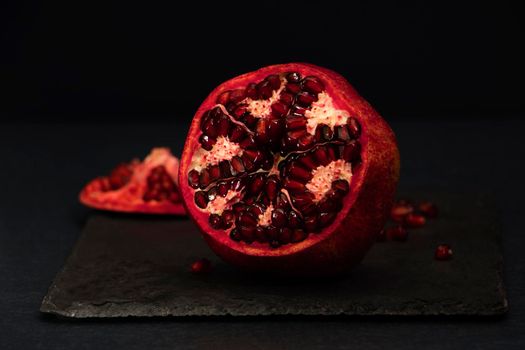 Fresh tasty sweet peeled pomegranate with red seeds on dark black background, macro angle view. pomegranate seeds . High quality photo