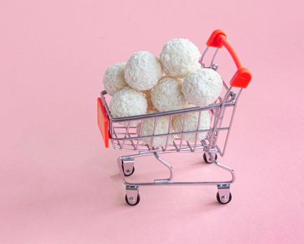 coconut round candies in a mini shopping basket, isolate on a pinc background. Supermarket shopping concept. full cart of sweets. High quality photo