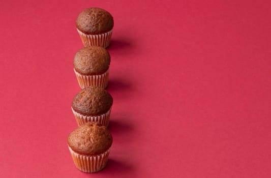 fresh mini cupcakes stand in a row on a red background. Muffins in paper forms. Confectionery background concept. Place for text. High quality photo