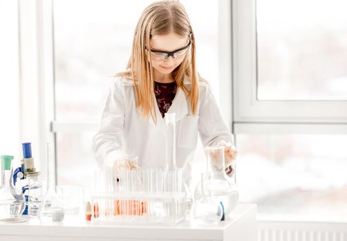 Smart girl doing scientific chemistry experiment wearing protection glasses. Schoolgirl with chemical equipment on school lesson