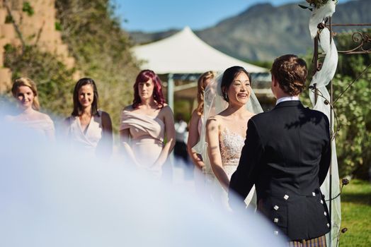 Shot of a cheerful young bride and groom holding each others hands at the wedding alter outside during the day.