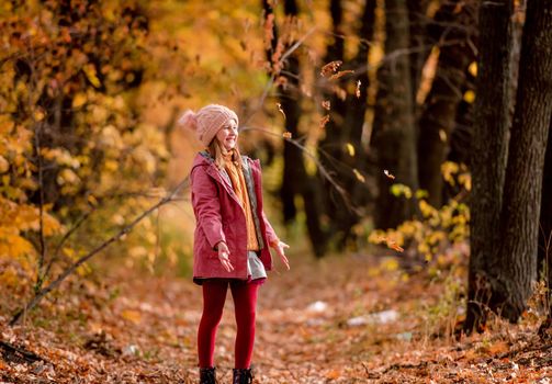 Preteen girl kid looking at fallen yellow leaves at autumn park. Beautiful portrait of child outdoors at nature