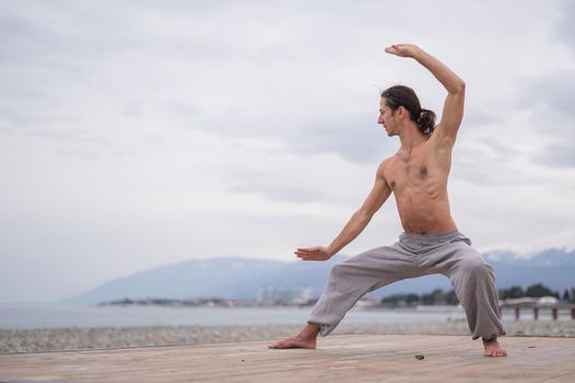 Caucasian man with naked torso practicing wushu on the seashore