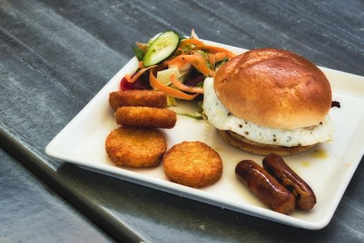 Breakfast brioche with fried egg, sausages, hash browns and salad