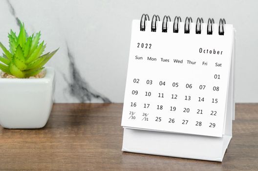 The October 2022 desk calendar with plant pot on wooden table.