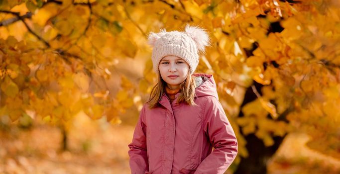 Preteen girl kid at autumn park with yellow leaves standing and looking at camera. Beautiful portrait of child outdoors at nature