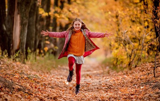 Hsppy girl kid running and jumping at autumn park with yellow trees. Beautiful kid outdoors
