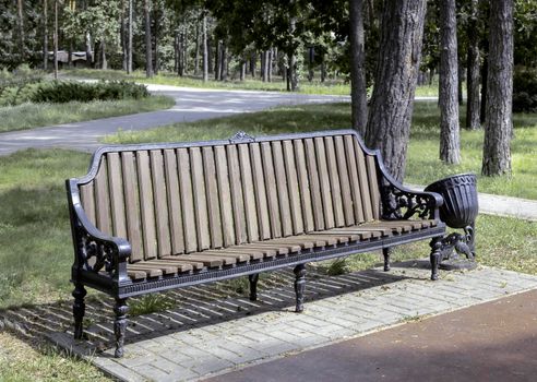 On the alley of the park there is a comfortable wooden bench for relaxing. Front view, close-up.