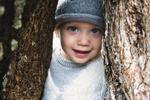 Close up of beautiful young girl model smiling and peering through a gap between tree trunks in the woods wearing winter clothes