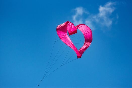A pink  heart-shaped kite flying in the air against a clear blue sky background
