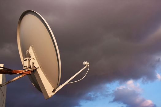 Satellite dish on a rooftop against a cloudy moody sky background