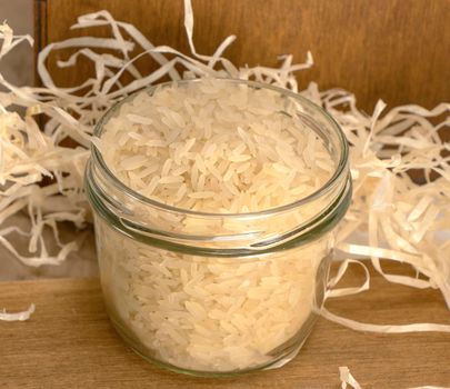 rice groats in a glass jar stands on a wooden surface against the background of paper shavings, piece hay, straw. dry, raw rice. High quality photo