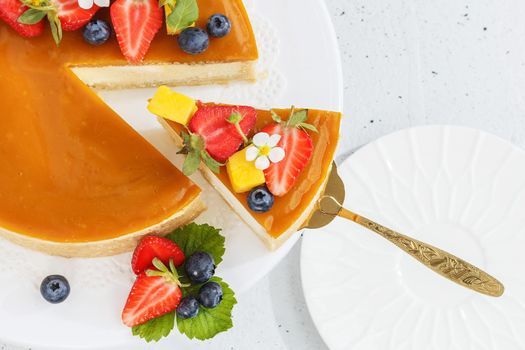 A piece of sliced mango cheesecake on a stand, garnished with berries and flowers. Healthy dessert. Vegetarian food.