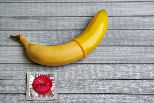 Red Condom and yellow banana lays on a gray wooden background