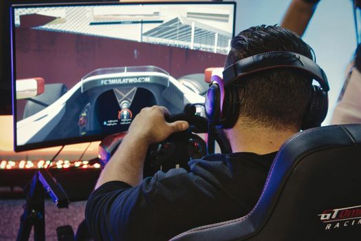 Mosta / Malta - May 11, 2019: A man playing a virtual reality racing game with steering wheel and headphones at a gadget fair