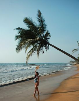 young woman stands under a palm tree on the beach . The concept of vacation and travel to the ocean. Resort on the island. High quality photo