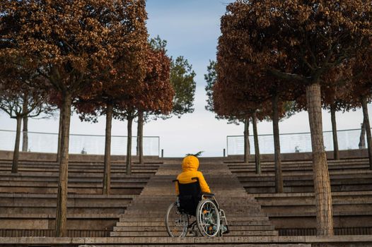 Woman in a wheelchair in front of the stairs in the street in winter