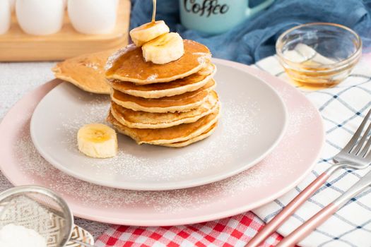 homemade banana pancakes on plate sprinkled powder and honey. Pancakes on the kitchen table against the background of eggs and cups with coffee. Pancake slide with honey topping and fresh bananas