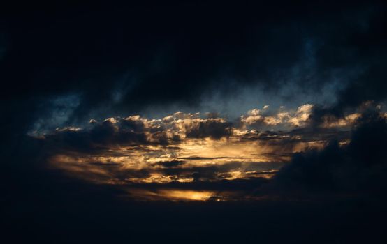 Dramatic dark evening sky landscape with moody clouds and golden sunlight