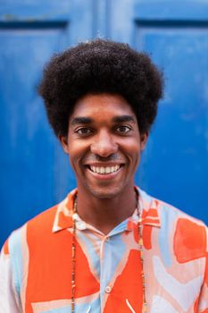 Vertical portrait of smiling young African American man with afro hairstyle looking at camera. Lifestyle concept.