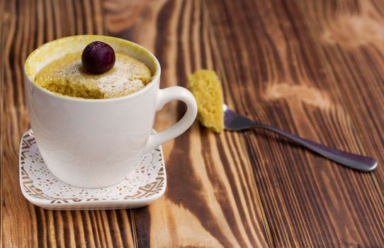 mini cupcake in a mug with a cherry on top. The piece is broken off on a fork. the muffin is cooked in a cup and ready to eat. Sweet dessert in a cup. Wooden background. High quality photo