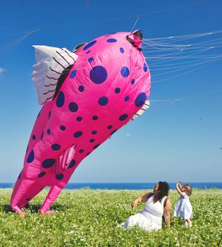 A mother and daughter sitting on the grass next to a kite in the shape of a puffer-fish
