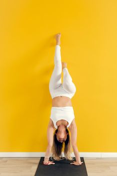 Yogini practicing yoga pose in the gym. The woman stands upside down.