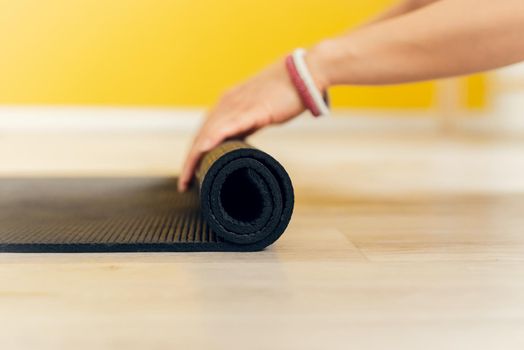 Close-up of an attractive young woman folding a black yoga or fitness mat after a workout. Healthy lifestyle, keep fit concept