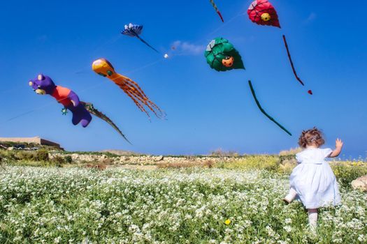 A little girl running through a field with kites flying against a clear blue sky