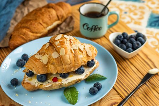 classic american breakfast. Fresh french croissant with fresh berries. blueberry and strawberry on cream cheese. Croissant and a cup with the inscription coffee on wooden background. Healthy breakfast