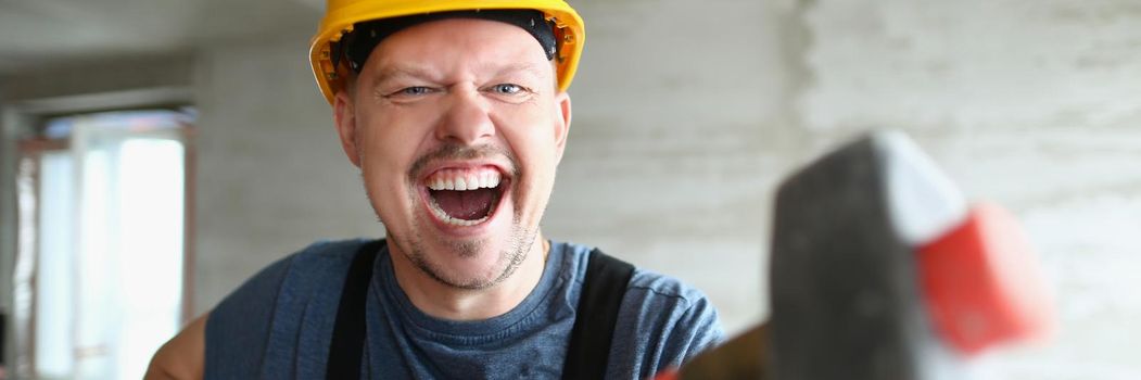 Builder man with a long hammer in his hands, close-up. Disassembly with a sledgehammer. Building renovation, cheerful handyman