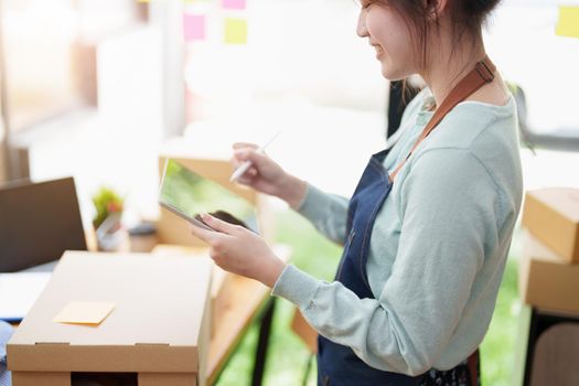 A portrait of a small startup, an SME owner, an Asian female entrepreneur checking orders to arrange the produce before packing the products in the inner boxes with the customers. Freelance concepts.