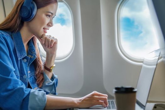 Travel, Portrait of a smiling Asian female tourist while listening to music and using a computer while on the plane.