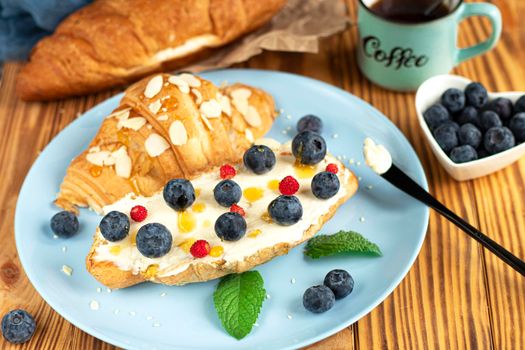 classic american breakfast. Fresh french croissant with fresh berries. blueberry and strawberry on cream cheese. Croissant and a cup with the inscription coffee on wooden background. Healthy breakfast