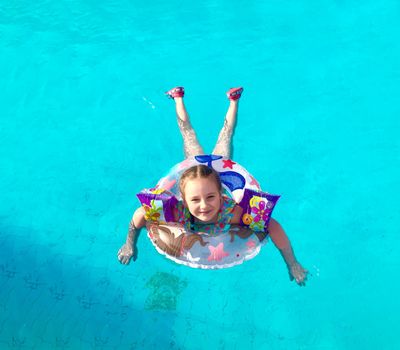 Child in swimming pool on inflatable multicolored ring. Little girl learning to swim with float. Water toy for baby and toddler. Healthy outdoor sport activity for children. Kids beach fun