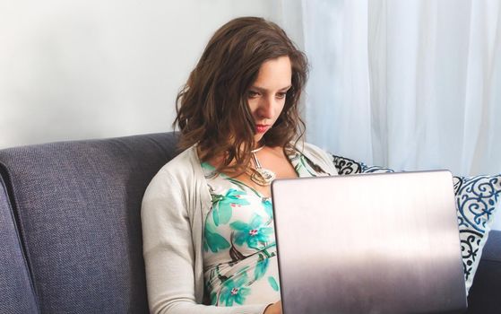 A young attractive white caucasian woman sitting on a sofa using a laptop computer