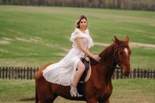 A woman in a white sundress riding a horse in a field.