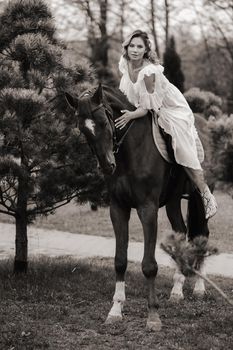 A woman in a white sundress riding a horse near a farm. black and white photo.