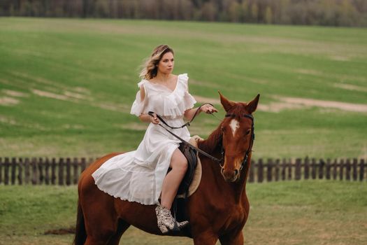 A woman in a white sundress riding a horse in a field.