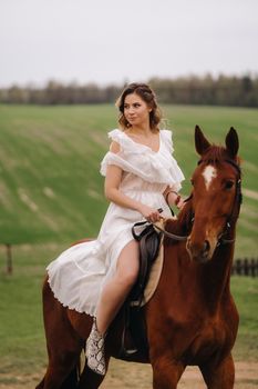 A woman in a white sundress riding a horse in a field.