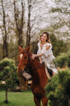 A woman in a white sundress riding a horse near a farm.