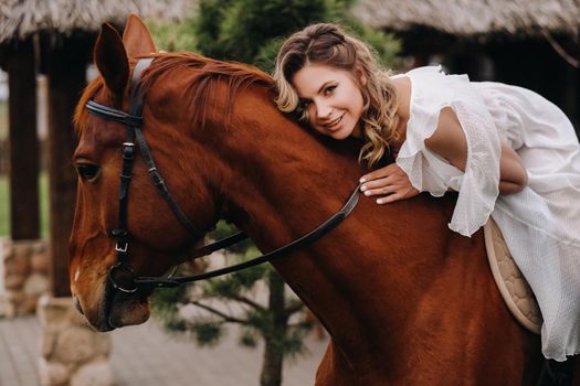 A woman in a white sundress riding a horse near a farm.