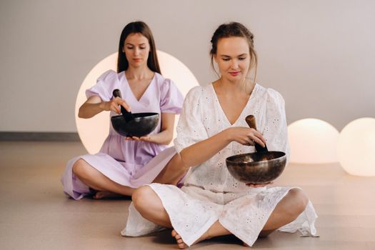 Two female yoga teachers playing a Tibetan bowl in the gym during a yoga retreat.