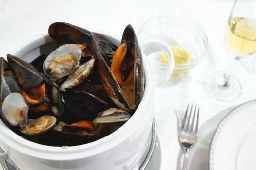 Pot of mussels and clams on a table isolated against a white tablecloth in a restaurant