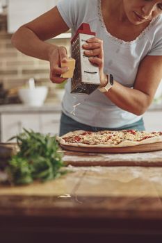 Young lady prepares homemade pizza by adding grated cheese before baking it in the oven