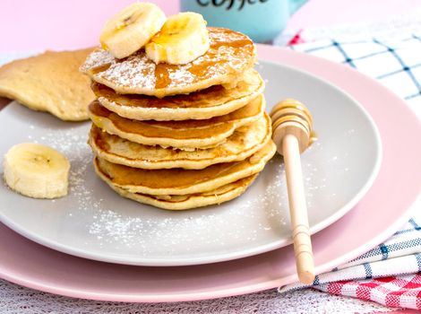 homemade banana pancakes on plate sprinkled powder and honey. Pancakes on the kitchen table against the background of eggs and cups with coffee. Pancake slide with honey topping and fresh bananas